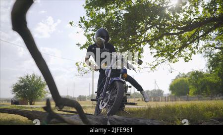 Brutal young man in sunglasses, blue sits on a custom motorcycle on the field with a black helmet. Motorcyclist on the meadow in the summer Stock Photo