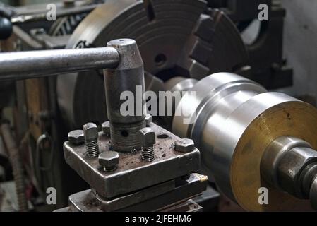 Closeup of a metal shaft parts cutting by old Lathe Machinery. lathe chuck and key 4-jaw screw chuck. Vintage Industrial Machinery in a old factory. Stock Photo