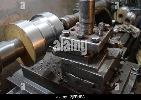 Closeup of a metal shaft parts cutting by old Lathe Machinery. lathe chuck and key 4-jaw screw chuck. Vintage Industrial Machinery in a old factory. Stock Photo