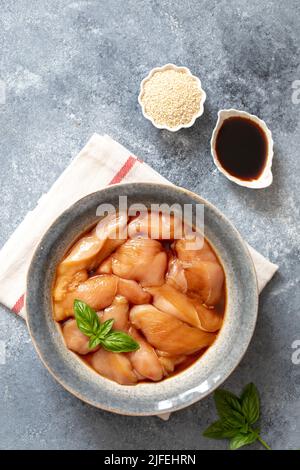 Raw diet marinated chicken meat with teriyaki sauce in a grey bowl. Marinating meat for cooking barbecue Stock Photo