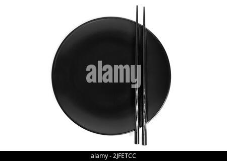 Pair of black lacquered chopsticks placed on a matte black plate isolated on white background, top-view. Stock Photo