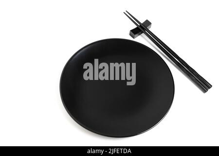 Pair of black lacquered chopsticks placed by a black plate isolated on white background. Stock Photo