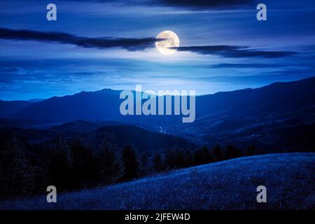 landscape of carpathian countryside at night. early autumn season in mountains in full moon light. trees on the grassy hills rolling in to the distant Stock Photo