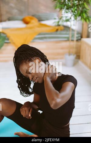 Vertical dark skin multiracial woman with dreads stretching, do yoga exercises. Female feel pain in neck joints, muscles Stock Photo