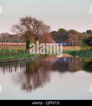 Maritime livery DB Cargo rail UK class 66 locomotive passing Catterall and the Lancaster canal with a freight train carrying lime. Stock Photo