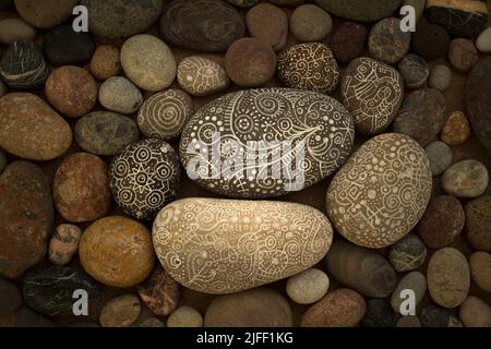 Set of pebbles in the sand of the beach at sunset with some stones painted with white lines and ethnic and symbolic drawings creating a scene of zen t Stock Photo