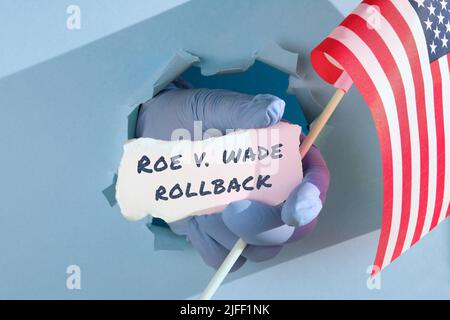 Text Roe vs Wade Rollback on scrap of paper. Medics, doctors hand in glove holding USA american flag and scrap of paper Stock Photo