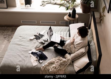 A pregnant woman is lying on the bed in front of a laptop and watching a nice movie. The concept of a pleasant time at home. Soft focus. Top view. Stock Photo