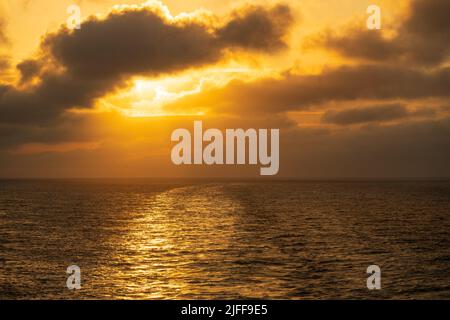 Setting sun illuminating the clouds over the wake of a cruise ship sailing down the coastline of Alaska Stock Photo