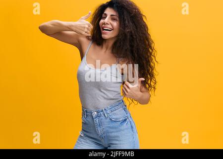 COOL OFFER. Enjoyed pretty Latin female with afro gesture thumb up, have good idea, cool mood, smile to you, stay isolated over yellow background Stock Photo