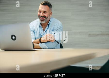 Happy mature businessman attending an online meeting with his business associates. Cheerful entrepreneur having a video conference while working remot Stock Photo