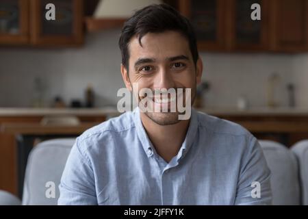 Hispanic man sit on sofa at home look at camera Stock Photo