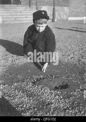 1940s summer. A boy outdoors playing marbles. An old fashioned game where the goal is to hit the pyramid of marbles with just one marble. If you hit, you won the marbles in the pyramid, otherwise the marble was lost. There was also variants of the game.  Sweden April 1940 Kristoffersson ref 111-6 Stock Photo