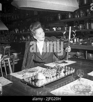 Shopping in the 1940s. Actress Greta Gynt, 1916-2000 in the store Svenskt tenn in Stockholm pictured holding a candle stick and with shelfes of decorative items for sale. The shop is highly specialized and famous for it's collections of decorative design that they produce themselves and imports from around the world. Svenskt tenn is still in business (2022)  Sweden 1946 ref X122-1 Stock Photo