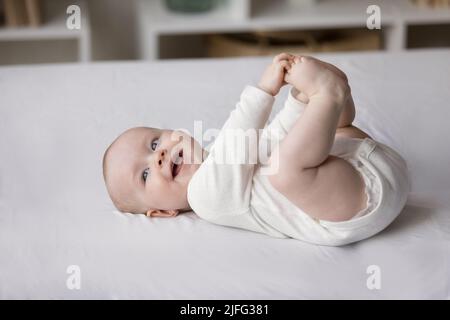 Smiling baby in bodysuit and diaper lying on bed, closeup Stock Photo