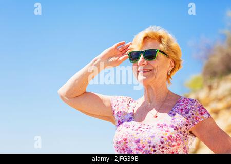 Elderly woman in sunglasses looking at the sea and having fan. Stock Photo