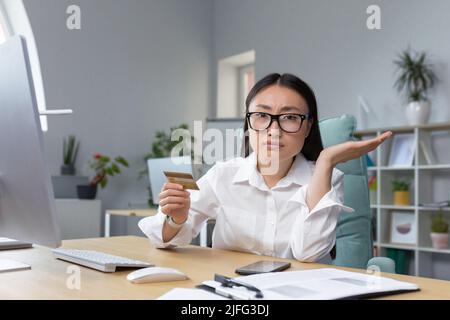 sad and disappointed asian woman trying to make a purchase in online store, business woman using phone and bank credit card, for bank transfers. Stock Photo