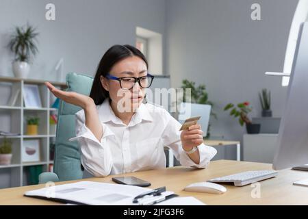 sad and disappointed asian woman trying to make a purchase in online store, business woman using phone and bank credit card, for bank transfers. Stock Photo