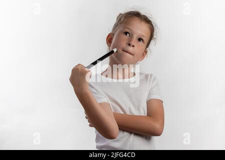 Girl magician with a magic wand in her hands - young magician thinking what to do next - against white background Stock Photo