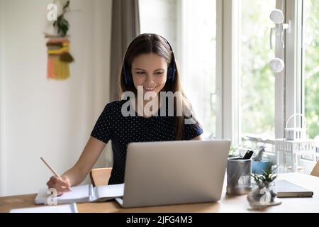 Happy engaged young female student in wireless headphones watching webinar Stock Photo