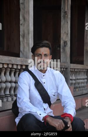 A good looking Indian young guy looking at camera while sitting on temple stairs Stock Photo