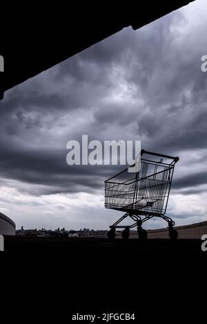 A shopping cart on a rooftop car park of an abandoned mall during the Coronavirus outbreak, dark rain clouds in the background. Stock Photo