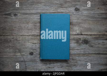 A closed book on an old wooden table. Blue hard cover. Vintage background. Stock Photo