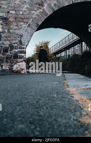 Stylish gangster man walking away, passing tunnel under a railway bridge  1920s theme. Fashionable brutal confident man. Stock Photo