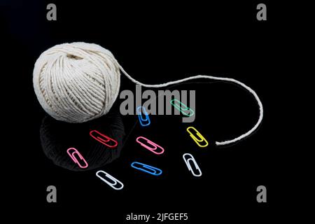 Ball of string and coloured paper clips isolated on a shiny black surface Stock Photo