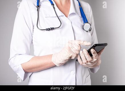 Doctor hands with phone. Telemedicine, using online technologies, medical application in smartphone for patient treatment concept. Woman in lab coat and gloves. High quality photo Stock Photo