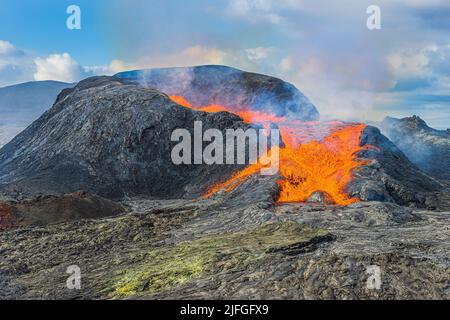 active volcano on the Reykjanes Peninsula. strong lava flow from a volcanic crater in Iceland. liquid magma at day in sunshine with clouds and blue sk Stock Photo