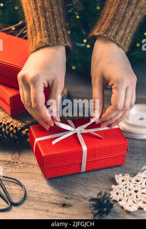Female hands decorating the red Christmas gift box with the white ribbon Stock Photo