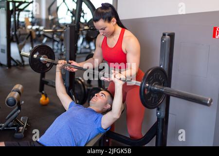 Young personal trainer helps to weak client doing bench press Stock Photo
