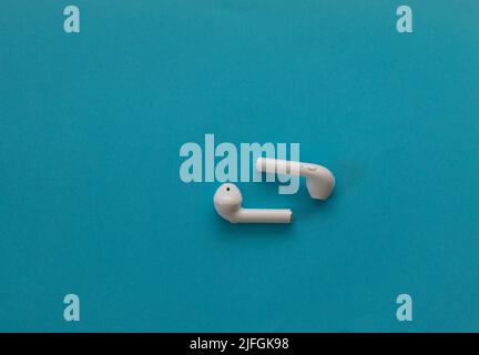 Small wireless headphones in white - on a blue background Stock Photo