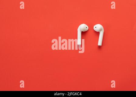 Small wireless headphones in white - on a red background Stock Photo