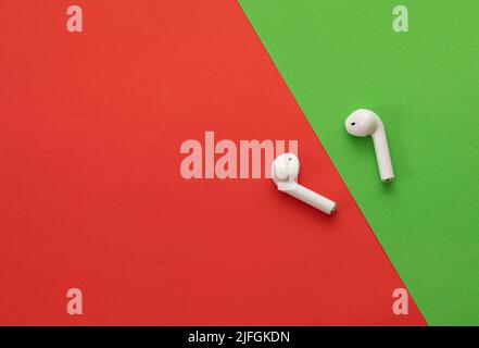 Small wireless headphones in white - on a red and green background Stock Photo