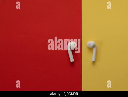 Small wireless headphones in white - on a red and yellow background Stock Photo