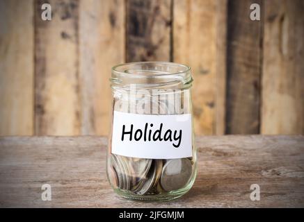 Coins in glass money jar with holiday label, financial concept. Vintage wooden background Stock Photo