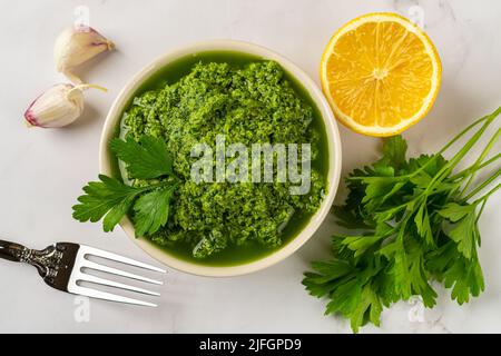 Fresh salsa verde in a bowl. Chimichurri dipping sauce from fresh parsley, garlic cloves, olive oil and lemon juice. Freshly made green sauce. Stock Photo