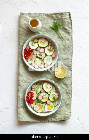 radish and cucumber salad served in a two bowls on the linen napkin and decorated with red currants, top view Stock Photo