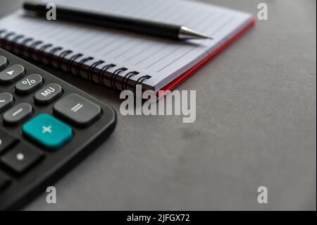 Calculator, pen, notepad lie on a gray surface. Open spring-loaded notebook with blank sheets. Close-up. Stock Photo