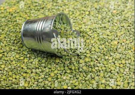 Dry split peas and a metal bucket. The tipped small bucket lies on top of the green uncooked beans. View from above at an angle. Selective focus. Stock Photo