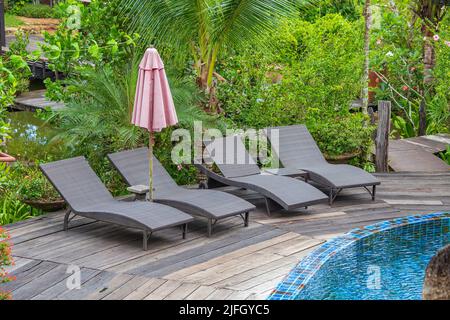 Swimming pool with relaxing beds and sun umbrella in tropical garden near beach in Thailand Stock Photo