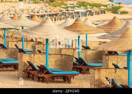 Sandy beach of the Red Sea with a group of straw umbrellas and deck chairs near Marsa Alam, Sahara desert, Egypt, Africa. Stock Photo