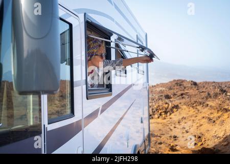 Woman opening caravan window in free parking outdoors admiring the nature outside. Travel and vehicle camper van destination for summer holiday vacati Stock Photo