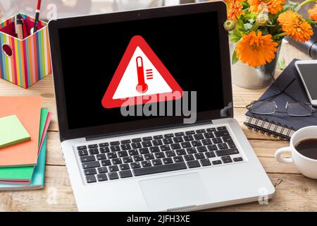 High temperature warning sign on a laptop screen.  Computer overheating concept. Heavy load and hot weather danger. Business office desk background. Stock Photo