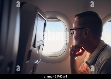 Portrait of man traveling by airplane. Passenger looking through plane window during flight Stock Photo