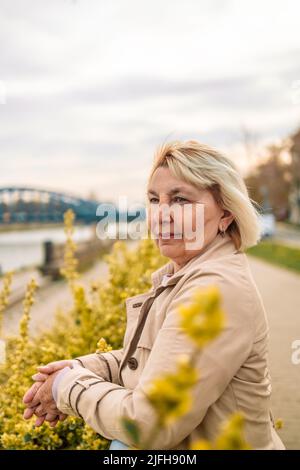 Outdoor portrait of beautiful and elegant middle age 55 - 60 year old woman in stylish clothes outside  Stock Photo