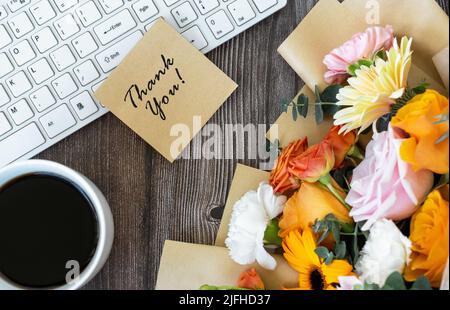 Thank you note on top of computer keyboard with cup of coffee and mixed flower bouquet Stock Photo