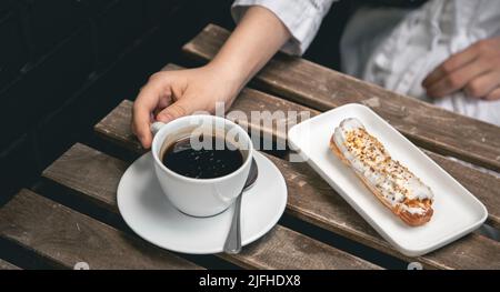 Cup of coffee and eclair on a wooden table close-up. Stock Photo